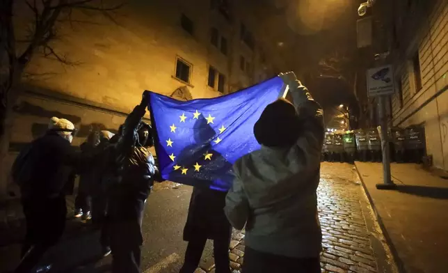 Demonstrators hold an EU flag in front of a police block rallying outside the parliament's building to continue protests against the government's decision to suspend negotiations on joining the European Union in Tbilisi, Georgia, on Monday, Dec. 2, 2024.(AP Photo/Zurab Tsertsvadze)