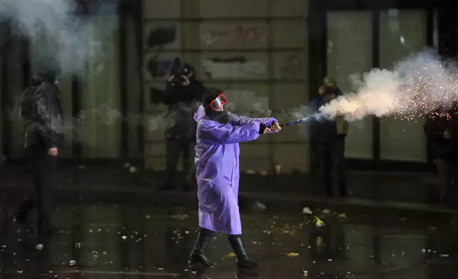 A demonstrator fires a firecracker towards police during a rally against the government's decision to suspend negotiations on joining the European Union for four years, outside the parliament's building in Tbilisi, Georgia, early Monday, Dec. 2, 2024. (AP Photo/Zurab Tsertsvadze)