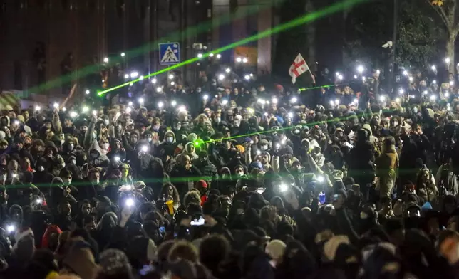 Protesters wave their lights as they are rallying outside the parliament's building to continue protests against the government's decision to suspend negotiations on joining the European Union in Tbilisi, Georgia, on Monday, Dec. 2, 2024.(AP Photo/Zurab Tsertsvadze)