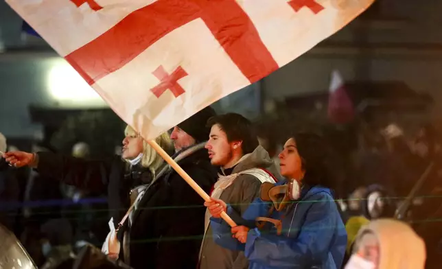 One of demonstrators holds a Georgian national flag in front of police who blocked a street to prevent protesters rallying against the governments' decision to suspend negotiations on joining the European Union for four years, outside the parliament's building in Tbilisi, Georgia, early Saturday, Nov. 30, 2024. (AP Photo/Zurab Tsertsvadze)