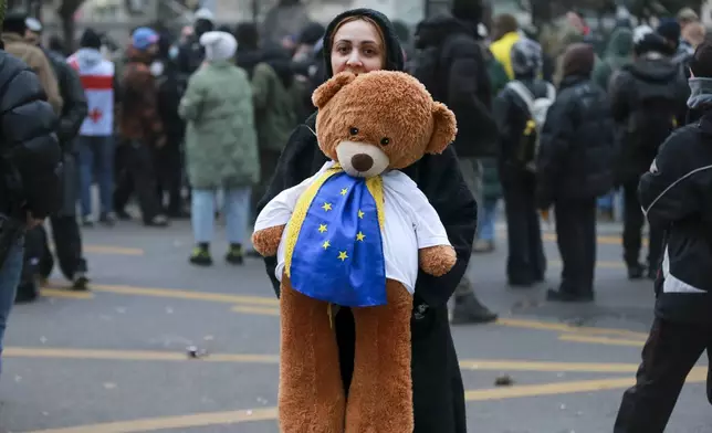 A woman holds a toy decorated with an EU and Ukrainian flags as protesters rally against the governments' decision to suspend negotiations on joining the European Union for four years, outside the parliament's building in Tbilisi, Georgia, early on Sunday, Dec. 1, 2024. (AP Photo/Zurab Tsertsvadze)