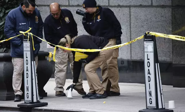 Members of the New York police crime scene unit pick up cups marking the spots where bullets lie as they investigate the scene outside the Hilton Hotel in midtown Manhattan where Brian Thompson, the CEO of UnitedHealthcare, was fatally shot Wednesday, Dec. 4, 2024, in New York. (AP Photo/Stefan Jeremiah)