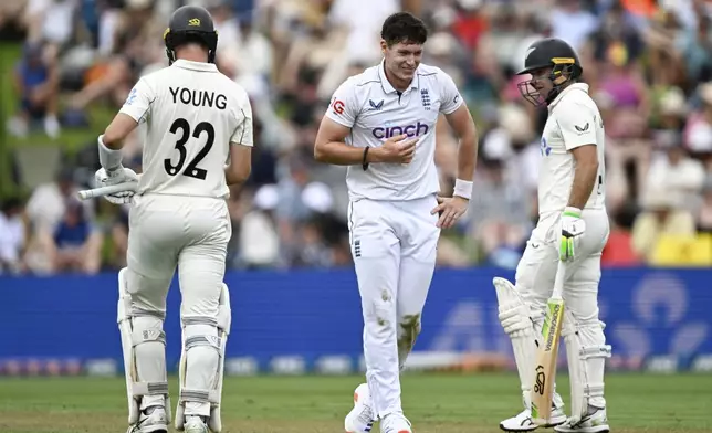 England bowler Matthew Potts, centre, reacts as he walks between New Zealand batsmen Will Young, left, and Tom Latham during during play on day one of the third cricket test between England and New Zealand in Hamilton, New Zealand, Saturday, Dec. 14, 2024. (Andrew Cornaga/Photosport via AP)