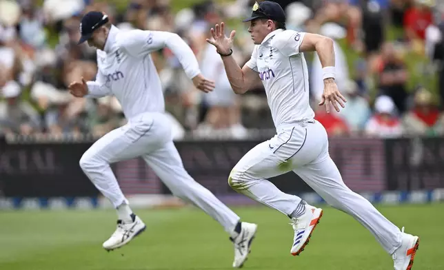 England's Matthew Potts, right, and Zak Crawley run after the ball during play on day one of the third cricket test between England and New Zealand in Hamilton, New Zealand, Saturday, Dec. 14, 2024. (Andrew Cornaga/Photosport via AP)