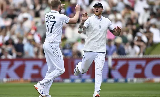 England's Gus Atkinson and Ben Stokes, right, celebrate the wicket of New Zealand's Will Young during play on day one of the third cricket test between England and New Zealand in Hamilton, New Zealand, Saturday, Dec. 14, 2024. (Andrew Cornaga/Photosport via AP)