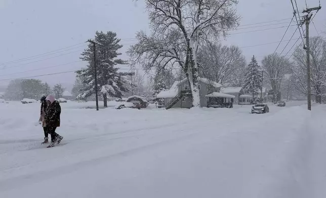 People walk in lake-effect snow on Sunday, Dec. 1, 2024, in Lowville, N.Y. (AP Photo/Cara Anna)