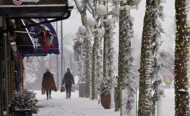 Shoppers walk through blowing and drifting snow, Monday, Dec. 2, 2024, in downtown St. Joseph, Mich. (Don Campbell/The Herald-Palladium via AP)