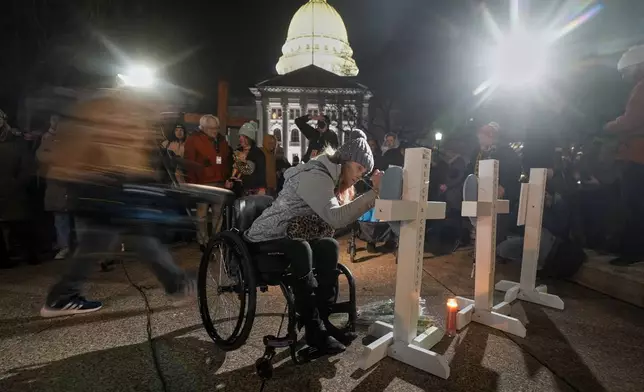 A supporter signs a cross during a candlelight vigil Tuesday, Dec. 17, 2024, outside the Wisconsin Capitol in Madison, Wis., following a shooting at the Abundant Life Christian School on Monday, Dec. 16. (AP Photo/Morry Gash)