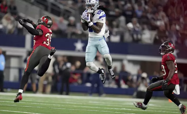 Dallas Cowboys wide receiver CeeDee Lamb (88) catches a pass between Tampa Bay Buccaneers cornerback Jamel Dean (35) and Christian Izien (29) in the first half of an NFL football game in Arlington, Texas, Sunday, Dec. 22, 2024. (AP Photo/Julio Cortez)