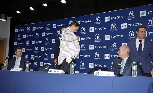 New York Yankees' Max Fried puts on a jersey as general manager Brian Cashman, right, and pitching coach Matt Blake, left, watch during a baseball news conference, Wednesday, Dec. 18, 2024, in New York. (AP Photo/Frank Franklin II)