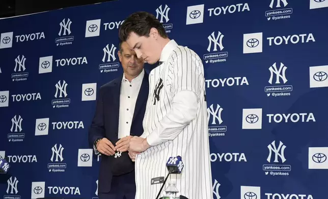 New York Yankees' Max Fried puts on a jersey as manager Aaron Boon, left watches during a baseball news conference, Wednesday, Dec. 18, 2024, in New York. (AP Photo/Frank Franklin II)