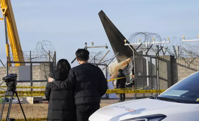 Mourners watch the site of a plane fire from outside of Muan International Airport in Muan, South Korea, Monday, Dec. 30, 2024. (AP Photo/Ahn Young-joon)