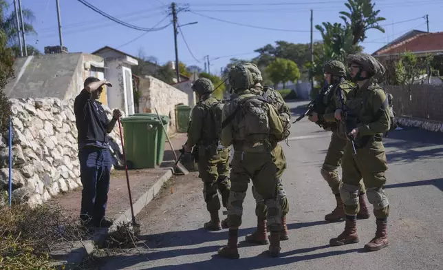 Rafi Shitrit speaks with soldiers patrolling the area as he cleans in front of his house during a visit for the day in the agricultural settlement of Avivim, next to the Lebanese border in upper Galilee, Israel, Monday Dec. 2, 2024. Israelis are still wary of returning to the north despite the ceasefire with Hezbollah.(AP Photo/Ohad Zwigenberg)