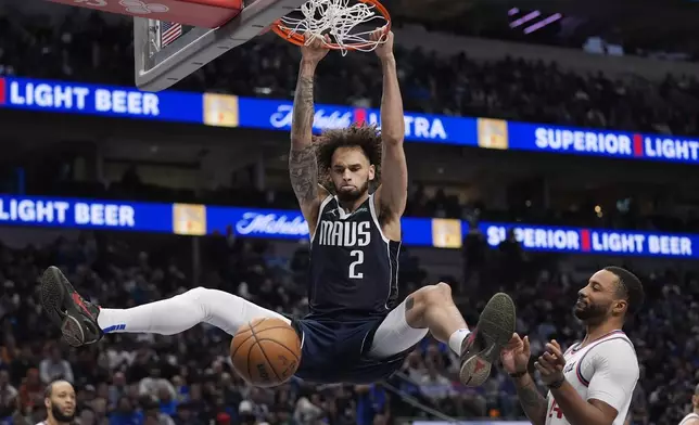 Dallas Mavericks center Dereck Lively II (2) hangs from the rim after slam-dunking against Los Angeles Clippers guard Norman Powell, right, during the second half of an NBA basketball game Saturday, Dec. 21, 2024, in Dallas. (AP Photo/LM Otero)