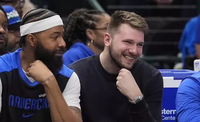 Dallas Mavericks guard Luka Doncic, right smiles while watching from the bench with forward Markieff Morris, left, during the first quarter of an NBA basketball game against the Los Angeles Clippers Saturday, Dec. 21, 2024, in Dallas. (AP Photo/LM Otero)