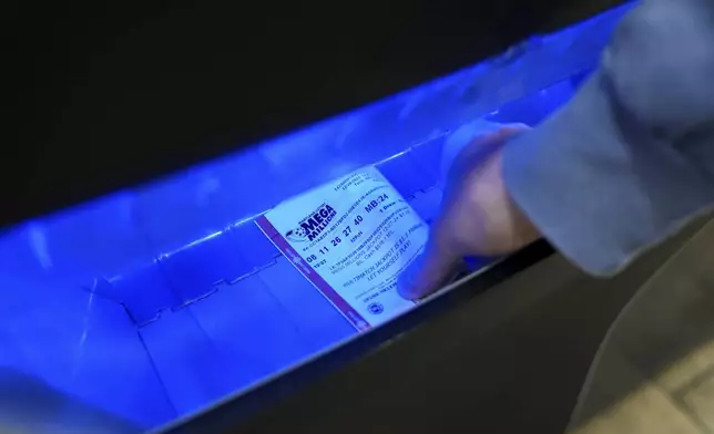 A person retrieves a Mega Millions lottery ticket from a self-serve terminal ahead of Friday's Mega Millions drawing of $1.15 billion, Thursday, Dec. 26, 2024, in Baltimore. (AP Photo/Stephanie Scarbrough)