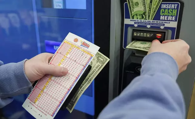 A person inserts cash into a self-serve terminal while holding their play slip ahead of Friday's Mega Millions drawing of $1.15 billion, Thursday, Dec. 26, 2024, in Baltimore. (AP Photo/Stephanie Scarbrough)