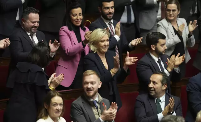 French far-right leader Marine Le Pen, center, applauds with other National Rally parliament members during conservative lawmaker Eric Ciotti's speech prior to a vote on a no-confidence motion that could bring him down and his cabinet for the first time since 1962, Wednesday, Dec. 4, 2024 the National Assembly in Paris. (AP Photo/Michel Euler)