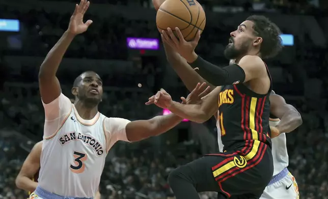 Atlanta Hawks guard Trae Young, right, attempts a layup against San Antonio Spurs guard Chris Paul (3) during the first half of an NBA basketball game in San Antonio, Thursday, Dec. 19, 2024. (AP Photo/Kin Man Hui)