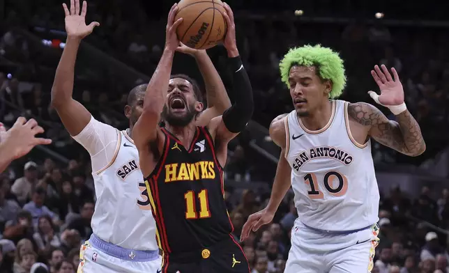 Atlanta Hawks guard Trae Young (11) reacts as he drives to the basket between San Antonio Spurs guard Chris Paul, left, and San Antonio Spurs forward Jeremy Sochan (10) during the first half of an NBA basketball game in San Antonio, Thursday, Dec. 19, 2024. (AP Photo/Kin Man Hui)