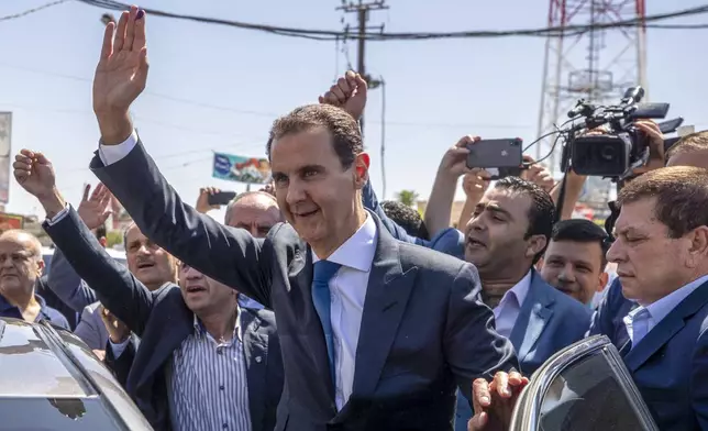 FILE - Then-President Bashar Assad, center, waves to his supporters at a polling station during presidential elections in the town of Douma, near the Syrian capital of Damascus, May 26, 2021. (AP Photo/Hassan Ammar, File)