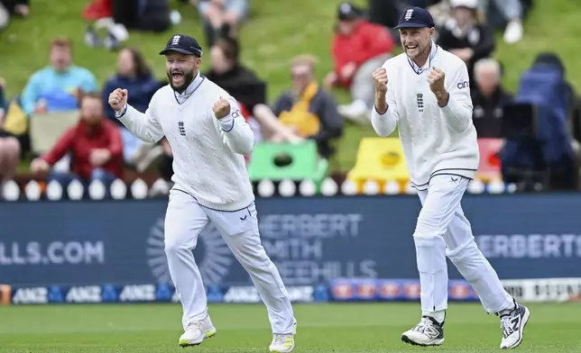 England fielders Ben Duckett, left, and Joe Root celebrate the dismissal of New Zealand's Daryl MItchell during play on day three of the second cricket test between New Zealand and England at the Basin Reserve in Wellington, New Zealand, Sunday, Dec.8, 2024. (Andrew Cornaga/Photosport via AP)