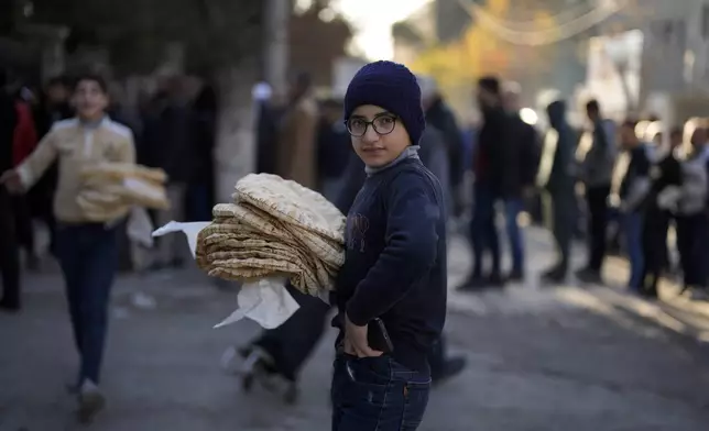 A Syrian boy look on as he carries bread in the city of Aleppo, Syria, Saturday, Dec. 14, 2024. (AP Photo/Khalil Hamra)