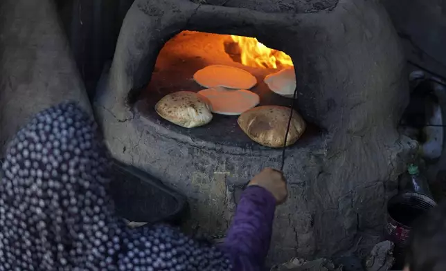 A Palestinian woman bakes bread in a clay oven amid dire food shortages in Deir al-Balah, Gaza Strip, Monday, Dec. 2, 2024. (AP Photo/Abdel Kareem Hana)