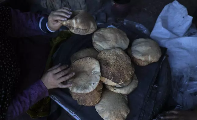 A Palestinian woman sorts through fresh bread amid dire food shortages in Deir al-Balah, Gaza Strip, Monday, Dec. 2, 2024. (AP Photo/Abdel Kareem Hana)