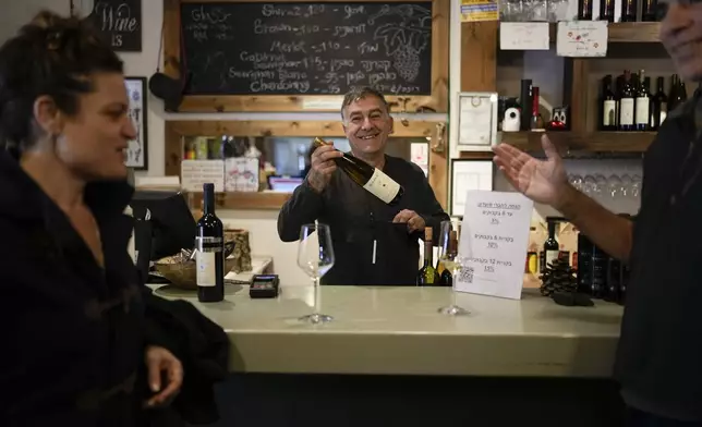 Ofer Bahat sells a bottle of wine to Shlomo Benhaim at his Bahat winery in the kibbutz of Ein Zivan in the Israeli-annexed Golan Heights, which most of the world considers occupied Syrian territory, Thursday, Dec. 19, 2024. (AP Photo/Matias Delacroix)