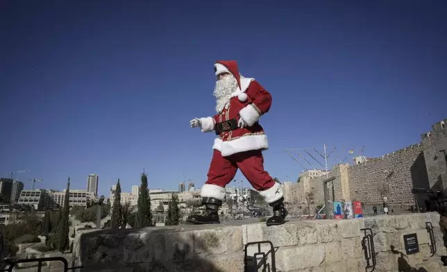 dressed as Santa Claus, walks along a wall next to the Old City of Jerusalem, ahead of the Christmas holiday, Thursday, Dec. 19, 2024.(AP Photo/Mahmoud Illean)