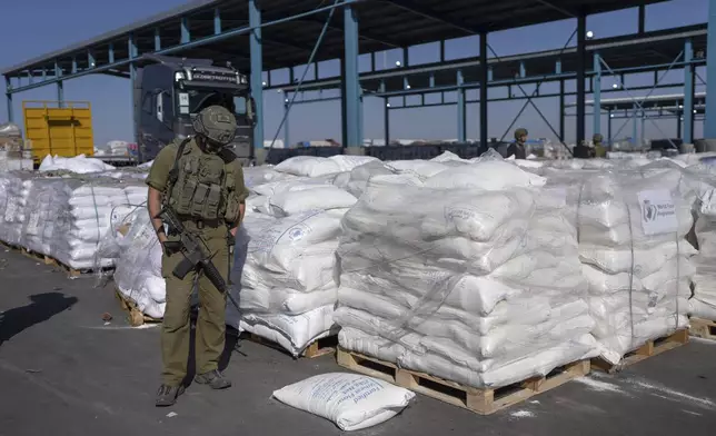 An Israeli soldier stands guard on the Palestinian side of the Kerem Shalom aid crossing as reporters tour the area where aid awaits pickup in the Gaza Strip, Thursday, Dec. 19, 2024. (AP Photo/Ohad Zwigenberg)