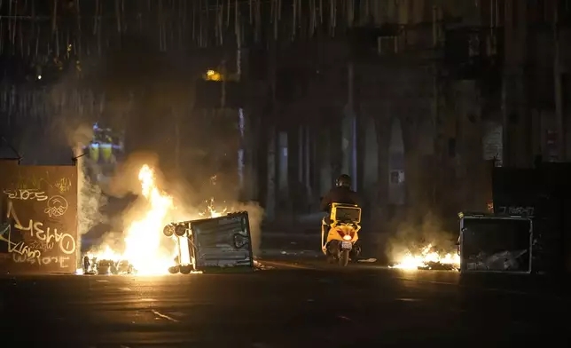 A motorcyclist passes a burning barricade during a rally to protest against the government's decision to suspend negotiations on joining the European Union in Tbilisi, Georgia, early Wednesday, Dec. 4, 2024. (AP Photo/Pavel Bednyakov)