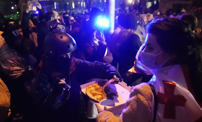 A woman distributes pizza to demonstrators during a rally outside the parliament's building to protests against the government's decision to suspend negotiations on joining the European Union, in Tbilisi, Georgia, Wednesday, Dec. 4, 2024. (AP Photo/Pavel Bednyakov)