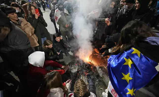 Demonstrators warm themselves by the fire during a rally outside the parliament against the government's decision to suspend negotiations on joining the European Union in Tbilisi, Georgia, on Wednesday, Dec. 4, 2024. (AP Photo/Pavel Bednyakov)