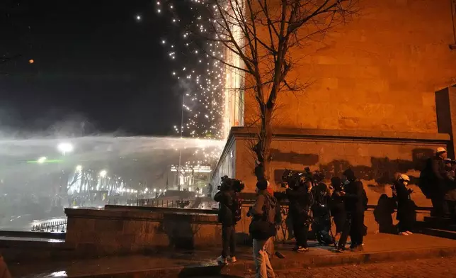 Journalists take cover around the corner of the parliament building during a protest against the government's decision to suspend negotiations on joining the European Union in Tbilisi, Georgia, on Tuesday, Dec. 3, 2024. (AP Photo/Pavel Bednyakov)