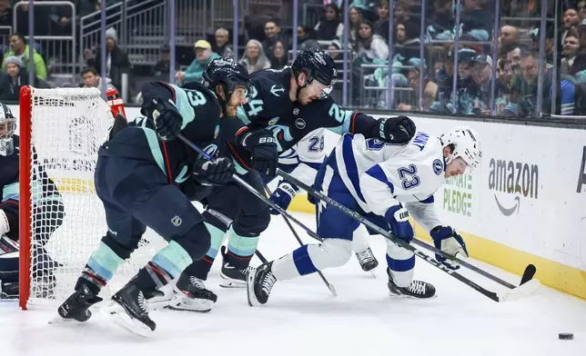 Seattle Kraken left wing Brandon Tanev, left, defenseman Jamie Oleksiak, center, and Tampa Bay Lightning center Michael Eyssimont, right, fight for the puck during the first period of an NHL hockey game Saturday, Dec. 14, 2024, in Seattle. (AP Photo/Maddy Grassy)