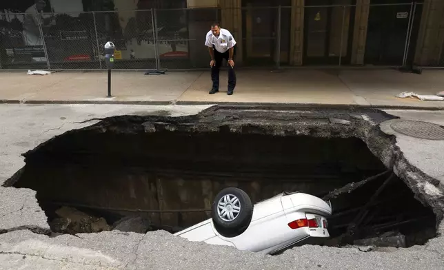 FILE - A St. Louis police officer looks over a large hole in 6th Street, Thursday, June 29, 2017, in St. Louis, that swallowed a Toyota Camry between Olive and Locust Streets. (Christian Gooden/St. Louis Post-Dispatch via AP, File)