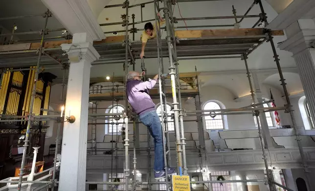 Conservator Corrine Long, of Dover, N.H., top, hands equipment to conservator Gianfranco Pocobene, of Malden, Mass., center, as they climb down scaffolding after working to restore nearly 300-year-old painted angels on the walls of the Old North Church, Wednesday, Dec. 18, 2024, in Boston. (AP Photo/Steven Senne)