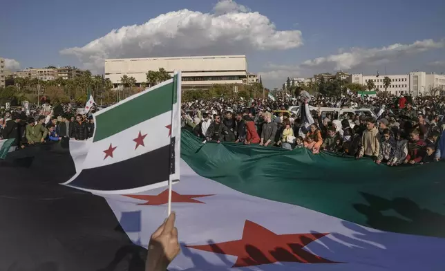 Syrians display a giant "revolutionary" Syrian flag during a celebratory demonstration following the first Friday prayers since Bashar Assad's ouster, in Damascus' central square, Syria, Friday, Dec. 13, 2024. (AP Photo/Leo Correa)