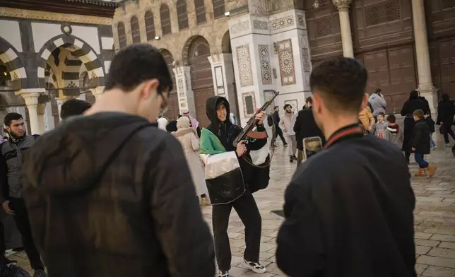 A young man poses holding a gun before Friday prayer at the Umayyad mosque in Damascus, Syria, Friday, Dec. 13, 2024. (AP Photo/Leo Correa)