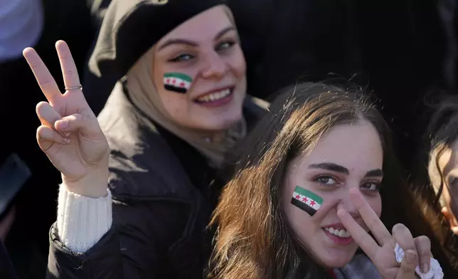 Syrian women flash victory signs with the colour of "revolutionary" Syrian flag on their faces, during a celebratory demonstration following the first Friday prayers since Bashar Assad's ouster, in Damascus' central square, Syria, Friday, Dec. 13, 2024. (AP Photo/Hussein Malla)