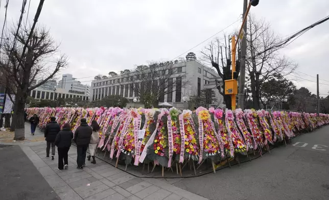 People walk past wreaths sent by supporters of impeached South Korean President Yoon Suk Yeol outside of the Constitutional Court in Seoul, South Korea, Friday, Dec. 20, 2024. (AP Photo/Ahn Young-joon)