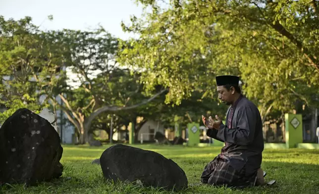 A man prays at a mass grave of victims of the 2004 Indian Ocean tsunami in Banda Aceh, Indonesia, Thursday, Dec. 26, 2024. (AP Photo/Reza Saifullah)