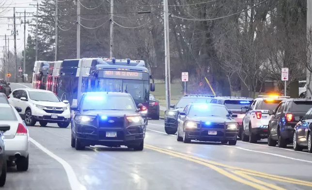 Bus carrying students leave as emergency vehicles are parked outside the Abundant Life Christian School in Madison, Wis., where multiple injuries were reported following a shooting, Monday, Dec. 16, 2024. (AP Photo/Morry Gash)