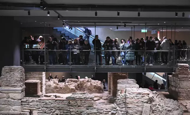 Commuters stand around an archaeological site located inside the Venizelou metro station during the inauguration day of the Thessaloniki metro, in Thessaloniki, northern Greece, Saturday, Nov. 30, 2024. (AP Photo/Giannis Papanikos)