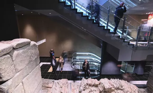 Commuters make their way around an archaeological site located inside the Venizelou metro station during the inauguration day of the Thessaloniki metro, in Thessaloniki, northern Greece, Saturday, Nov. 30, 2024. (AP Photo/Giannis Papanikos)