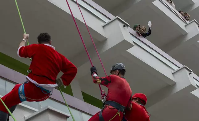 A mother holds her child from a hospital balcony to see Kosovo alpinists disguised as super-heroes of modern times descending with ropes from a hospital roof offering gifts to little children in Pristina hospital on Friday, Dec. 13, 2024. (AP Photo/Visar Kryeziu)