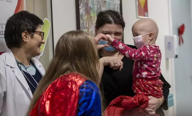 Kosovo alpinists disguised as super-heroes of modern times delivers New Year's gifts and makes a love sign with a patient wearing a mask in Pristina hospital on Friday, Dec. 13, 2024. (AP Photo/Visar Kryeziu)