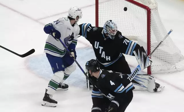 Utah Hockey Club goaltender Karel Vejmelka (70) is scores against by Vancouver Canucks left wing Danton Heinen, as teammate Vancouver Canucks center Pius Suter (24) looks on during the second period of an NHL hockey game Wednesday, Dec. 18, 2024, in Salt Lake City. (AP Photo/Rick Bowmer)